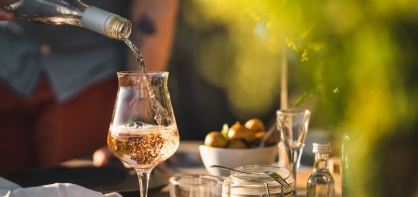 A man pouring a glass of wine under his garden pergola. 